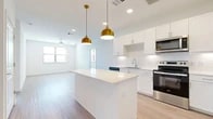 This single-floor residence offers a thoughtfully designed layout across two bedrooms and two bathrooms. The open-concept kitchen and living area serves as the heart of the home, featuring white shaker-style cabinetry, a white quartz countertop island, a classic subway tile backsplash, and a full suite of stainless steel appliances. A pair of gold pendant lights above the island adds a warm, contemporary accent to the clean, bright space. Light wood-look flooring extends throughout the main living area, enhancing the airy feel.

The living room flows naturally from the kitchen and is illuminated by multiple windows and a ceiling fan, creating a comfortable and well-lit environment. Both bedrooms are generously sized, with the primary bedroom offering plush carpeting, a ceiling fan, and a natural window view. The second bedroom features light wood-look flooring and its own window for natural light.

The primary bathroom is notably spacious, with a wide vanity, a tub-shower combination, wood-look flooring, recessed lighting, and direct access to a walk-in closet. The second bathroom is clean and functional, featuring a white vanity with chrome hardware and matching flooring. Each room reflects a consistent, neutral design palette that maximizes brightness and lends itself to a variety of interior styles.
