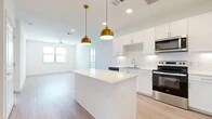 This single-floor residence offers a thoughtfully designed layout across two bedrooms and two bathrooms. The open-concept kitchen and living area serves as the heart of the home, featuring white shaker-style cabinetry, a white quartz countertop island, a classic subway tile backsplash, and a full suite of stainless steel appliances. A pair of gold pendant lights above the island adds a warm, contemporary accent to the clean, bright space. Light wood-look flooring extends throughout the main living area, enhancing the airy feel.

The living room flows naturally from the kitchen and is illuminated by multiple windows and a ceiling fan, creating a comfortable and well-lit environment. Both bedrooms are generously sized, with the primary bedroom offering plush carpeting, a ceiling fan, and a natural window view. The second bedroom features light wood-look flooring and its own window for natural light.

The primary bathroom is notably spacious, with a wide vanity, a tub-shower combination, wood-look flooring, recessed lighting, and direct access to a walk-in closet. The second bathroom is clean and functional, featuring a white vanity with chrome hardware and matching flooring. Each room reflects a consistent, neutral design palette that maximizes brightness and lends itself to a variety of interior styles.