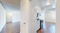 Located at 2070 N Beverly Plaza in Long Beach, CA, this single-floor residence offers six bedrooms and two bathrooms across a generously sized floor plan. The open living area makes a strong first impression with rich hardwood-style flooring, a textured ceiling, and wide vertical-blind-covered sliding doors that flood the space with natural light. The galley-style kitchen is well-appointed with white cabinetry, granite-look countertops, black appliances including an electric range, built-in microwave, and dishwasher, all complemented by matching hardwood-style floors. Three hallways connect the various rooms, providing an efficient and organized flow throughout the unit. The six bedrooms are finished with plush carpeting and sliding closet doors offering built-in storage, creating comfortable and functional private spaces. The primary bedroom is generously proportioned with ample room for furnishings. Both bathrooms feature white vanity cabinetry with stone-look countertops, undermount sinks, large mirrors, and hardwood-style flooring. One bathroom includes a glass-enclosed shower, while the other offers a shower-tub combination. The overall aesthetic is clean and bright, with a neutral palette of whites and warm wood tones throughout.