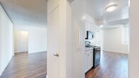 Located at 2070 N Beverly Plaza in Long Beach, CA, this single-floor residence offers six bedrooms and two bathrooms across a generously sized floor plan. The open living area makes a strong first impression with rich hardwood-style flooring, a textured ceiling, and wide vertical-blind-covered sliding doors that flood the space with natural light. The galley-style kitchen is well-appointed with white cabinetry, granite-look countertops, black appliances including an electric range, built-in microwave, and dishwasher, all complemented by matching hardwood-style floors. Three hallways connect the various rooms, providing an efficient and organized flow throughout the unit. The six bedrooms are finished with plush carpeting and sliding closet doors offering built-in storage, creating comfortable and functional private spaces. The primary bedroom is generously proportioned with ample room for furnishings. Both bathrooms feature white vanity cabinetry with stone-look countertops, undermount sinks, large mirrors, and hardwood-style flooring. One bathroom includes a glass-enclosed shower, while the other offers a shower-tub combination. The overall aesthetic is clean and bright, with a neutral palette of whites and warm wood tones throughout.