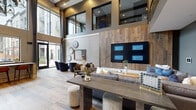Located in Centennial, CO, this contemporary clubhouse offers a generously sized, single-floor gathering space defined by striking architectural design and upscale finishes throughout. The main living area commands attention with soaring double-height ceilings, exposed beams, and a dramatic wood-paneled feature wall housing a multi-screen display. Wood-look tile flooring flows throughout the open-plan interior, complementing the warm, neutral palette. Comfortable lounge seating arrangements provide multiple social zones, while a sleek central table with bar stools offers an additional gathering point. A modern staircase with glass railings and metal detailing leads to an open mezzanine level overlooking the main floor. The game room features a billiards table, shuffleboard, and patterned carpet tiles, with floor-to-ceiling windows framing views of an outdoor courtyard. Large sliding glass doors and expansive glazing flood the space with natural light, seamlessly connecting the interior to the exterior patio. The entry foyer is anchored by a cozy seating vignette beneath the open stairwell. Throughout, curated décor, layered lighting, and thoughtful furnishings create a polished yet inviting ambiance suited for community gatherings and everyday socializing.