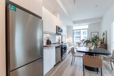 Located at 200 Deerfield Rd in Newmarket, Ontario, this modern 2-bedroom, 1-bathroom unit offers a thoughtfully designed open-concept layout finished in a clean, contemporary palette. Light wood flooring runs throughout, complementing crisp white walls and creating a bright, cohesive atmosphere.

The combined kitchen and living area forms the heart of the unit. The galley-style kitchen is outfitted with white flat-panel cabinetry, stainless steel appliances including a refrigerator, stove, dishwasher, and built-in microwave, along with a white tile backsplash and generous counter space. The living area flows naturally from the kitchen and dining space, benefiting from large sliding windows that bring in abundant natural light and views of the surrounding Newmarket cityscape and greenery.

The primary bedroom is a serene retreat featuring expansive floor-to-ceiling windows on two walls, offering sweeping views of the city and treetops, along with built-in sliding closet doors. The second bedroom also enjoys a large window with outdoor views, providing a comfortable and well-lit space. The full bathroom is finished with white tile, a combined tub and shower, and a clean vanity with ample storage. Every room reflects a consistent modern design sensibility, making this a well-appointed urban residence.