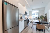 Located at 200 Deerfield Rd in Newmarket, Ontario, this modern 2-bedroom, 1-bathroom unit offers a thoughtfully designed open-concept layout finished in a clean, contemporary palette. Light wood flooring runs throughout, complementing crisp white walls and creating a bright, cohesive atmosphere.

The combined kitchen and living area forms the heart of the unit. The galley-style kitchen is outfitted with white flat-panel cabinetry, stainless steel appliances including a refrigerator, stove, dishwasher, and built-in microwave, along with a white tile backsplash and generous counter space. The living area flows naturally from the kitchen and dining space, benefiting from large sliding windows that bring in abundant natural light and views of the surrounding Newmarket cityscape and greenery.

The primary bedroom is a serene retreat featuring expansive floor-to-ceiling windows on two walls, offering sweeping views of the city and treetops, along with built-in sliding closet doors. The second bedroom also enjoys a large window with outdoor views, providing a comfortable and well-lit space. The full bathroom is finished with white tile, a combined tub and shower, and a clean vanity with ample storage. Every room reflects a consistent modern design sensibility, making this a well-appointed urban residence.