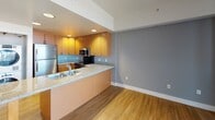 Located on the ninth floor at 1455 Kettner in San Diego, this single-level residence offers a well-organized layout with distinct living, kitchen, bedroom, and bathroom areas. A welcoming hallway finished with wood-style plank flooring leads toward the main living space, drawing the eye toward floor-to-ceiling windows that flood the interior with natural light and provide elevated city views.

The kitchen is thoughtfully designed with warm-toned cabinetry, stainless steel appliances including a refrigerator, range, and built-in microwave, complemented by granite-style countertops and a double stainless steel sink. Recessed lighting adds functionality, while a peninsula counter connects the kitchen to the open living area, which continues the wood-style flooring and features neutral gray accent walls.

The bedroom is carpeted for comfort and includes access to a walk-in closet area, providing generous storage. The bathroom features tile flooring, a tub-and-shower combination with sliding glass doors, a wood-toned vanity with granite-style countertop, a mirrored medicine cabinet, and a well-lit vanity fixture. Throughout the unit, clean lines, neutral tones, and consistent finishes create a cohesive and functional living environment.