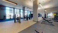 The fitness center at 880 Pacific St in Stamford, Connecticut, is a expansive, well-appointed facility designed to support a comprehensive workout experience. The space is flooded with natural light through floor-to-ceiling windows that frame striking panoramic views of the Stamford skyline, creating an energizing and open atmosphere throughout.

The main cardio zone features a row of Matrix treadmills and additional cardio machines aligned along the window wall, allowing users to exercise while taking in the urban views. Adjacent to this area, a generous strength training section is equipped with a wide selection of Matrix selectorized machines, free weights, benches, and functional training equipment, all arranged across durable, zone-specific flooring.

A dedicated studio space with large mirrored walls, neutral woven flooring, and a large display screen provides an ideal environment for group fitness, on-demand classes, or personal training sessions. Stability balls, plyo boxes, and suspension training equipment are readily available within this room. Glass partitions connect the studio to the main floor, maintaining an open and connected feel across the entire facility.

The center also features soaring ceilings with warm wood beam accents, pendant and linear lighting, built-in shelving, and motivational athletic photography, lending a polished, purposeful aesthetic. The layout ensures ample space for movement, making this a thoroughly equipped and thoughtfully designed fitness destination.