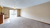 Located at 4320 Westbrook Dr in Ames, Iowa, this efficiently designed single-floor unit offers a thoughtful layout comprising a living room, kitchen, and full bathroom. The living room is a comfortable, carpeted space featuring a ceiling fan, a sliding glass door that opens to a balcony with outdoor views, and a closet with double doors — providing both functionality and natural light. The textured ceiling adds a classic residential touch throughout. The kitchen is well-appointed with warm wood cabinetry, granite-style countertops, a tile backsplash with a stone mosaic pattern, and black appliances including a refrigerator, microwave, and dishwasher. A built-in wine rack above the cabinetry adds a distinctive detail. Light hardwood flooring runs through the kitchen, creating a clean contrast to the carpeted living area. The bathroom is neatly finished with a full tub and shower surround in white, complemented by tile flooring, a toilet, and a vanity with granite-style countertops. The unit's neutral color palette of warm beiges and tans throughout creates a cohesive and inviting atmosphere, making efficient use of its compact footprint.