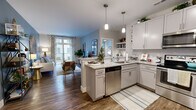 This thoughtfully designed single-floor residence offers three bedrooms and two full bathrooms across a comfortable and efficient layout. The open-concept kitchen and living area serves as the heart of the home, where wood-look flooring flows seamlessly throughout. The kitchen is outfitted with white shaker-style cabinetry extending to the ceiling, stainless steel appliances including a refrigerator, range, and microwave, a subway tile backsplash, and a granite-topped peninsula with bar seating for three — ideal for casual dining or entertaining. Pendant lighting adds a modern touch overhead. The living room features a bold blue accent wall, large windows, and sliding glass doors that open to a private balcony, filling the space with natural light and outdoor views. The primary bedroom is generously proportioned, featuring soft carpet, a soothing color palette, and a dedicated closet with a full rod system. The primary bathroom offers a wide vanity with ample storage, dark tile flooring, and an in-unit washer and dryer. The second bathroom mirrors the refined aesthetic with dark tile flooring, a single vanity, and clean, neutral wall tones throughout. The overall ambiance is modern, bright, and move-in ready.