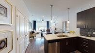Located at 11501 W 81st St in Lenexa, Kansas, this single-floor residence offers a thoughtfully designed open-concept layout that seamlessly connects the kitchen, dining, and living areas. The kitchen is a standout feature, equipped with stainless steel appliances, rich dark cabinetry, a textured tile backsplash, and a generous island with quartz countertops and pendant lighting — ideal for both cooking and casual dining. The living area is bright and welcoming, with large windows dressed in roller shades and navy drapes that allow ample natural light while offering outdoor views. Wood-style flooring flows through the main living spaces, adding warmth and cohesion. The residence includes two bedrooms, each with plush carpeting, ceiling fans, and large windows with outdoor views. The primary bedroom features a walk-in closet. Both bathrooms are finished with dark vanity cabinetry, quartz countertops, wood-style flooring, and tile surround. The primary bath includes a glass-enclosed walk-in shower with a dual-sink vanity, while the secondary bath offers a tub-shower combination. Throughout the home, clean white walls and modern fixtures contribute to a polished, contemporary aesthetic.