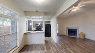 This single-floor residence offers a well-organized, open-concept layout designed for comfortable everyday living. The living area is a standout space, featuring rich hardwood-style flooring, a classic tile-surround fireplace, and a window that fills the room with natural light. A ceiling fan adds both function and charm to the area. The kitchen is efficiently designed with gray cabinetry, granite-style countertops, and black appliances including a refrigerator, electric range with microwave, and dishwasher. Pendant lighting illuminates the pass-through counter, which connects the kitchen to the main living and dining areas, creating an open and social atmosphere. A separate entry area features wood-look tile flooring and provides a clean transition into the home. The bedrooms are carpeted for warmth and comfort, with large windows that bring in natural light and views of the outdoors. The bathrooms are finished with granite-topped vanities, gray cabinetry, and wood-look tile flooring, maintaining a consistent aesthetic throughout. A laundry area is conveniently accessible from one of the bathrooms. Textured ceilings are present throughout the space, adding a classic residential character to every room.