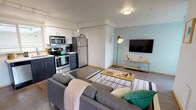 Located at 4717 Brooklyn Avenue NE in Seattle's University District, this contemporary single-floor unit offers a thoughtfully designed open-concept layout with modern finishes throughout. The living area features wood-look flooring, soft teal accent walls, and a wall-mounted TV, creating a comfortable and stylish atmosphere. A sliding glass door opens to a private balcony, bringing in natural light and offering views of the surrounding Seattle cityscape.

The kitchen is fully equipped with stainless steel appliances — including a refrigerator, range, microwave, and dishwasher — paired with two-tone cabinetry featuring dark lower and white upper cabinets, white countertops, and track lighting overhead.

The bedroom is a bright, well-proportioned retreat with floor-to-ceiling windows that frame expansive city views. A sliding closet provides convenient storage space, and the carpeted flooring adds warmth to the room.

The bathroom is clean and modern, featuring a large vanity with a white countertop, an oversized mirror, and a glass-enclosed walk-in shower. Tile flooring and contemporary fixtures complete the refined look. Overall, the unit presents a cohesive, urban aesthetic well-suited to the vibrant Seattle neighborhood it calls home.