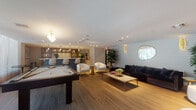 Located at 1005 Spring Garden Rd in Miami, FL, this single-floor amenity lounge is a thoughtfully designed social space that blends modern aesthetics with functional entertainment features. The open layout is unified by warm wood-tone tile flooring that flows seamlessly throughout, complemented by smooth white ceilings with recessed and track lighting that create a bright, welcoming atmosphere.

At the center of the space, a full-size pool table serves as a focal point for recreation. Adjacent to it, a dedicated wet bar area features warm wood cabinetry, a white quartz countertop, an integrated sink with gold-toned fixtures, and illuminated open shelving styled with decorative objects and greenery. Large windows along the bar wall invite natural light and views of the outdoors.

The lounge area is furnished with a plush dark sectional sofa accented by a patterned geometric wallcovering, gold wall sconces, and a round decorative mirror. White bouclé accent chairs paired with gold side tables add a refined touch, while a large flat-screen television mounted on the wall makes the space equally suited for viewing and relaxation. Tall indoor plants are distributed throughout, adding life and warmth. The overall ambiance is sophisticated yet inviting, making this lounge an ideal gathering space.