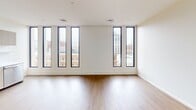 Located at Residences At 111 in the heart of downtown Grand Rapids, Michigan, Unit 819 K is a thoughtfully designed 520-square-foot studio apartment spanning a single floor. The open-concept layout seamlessly connects the living area and kitchen, maximizing the efficient use of space throughout.

The kitchen is a standout feature, outfitted with light wood-grain cabinetry that extends from floor to ceiling, offering generous storage. Stainless steel appliances — including a full-size refrigerator, electric range, dishwasher, and undermount sink — provide a complete, modern cooking space. Clean white countertops and light wood laminate flooring carry a consistent, contemporary aesthetic throughout.

The living area is bright and open, anchored by a striking row of tall, narrow black-framed windows that frame panoramic views of the Grand Rapids skyline and surrounding historic architecture. Recessed lighting illuminates the space evenly, complementing the natural light that flows in throughout the day.

Two hallways connect the main living areas to additional spaces, including a dedicated room ideal for a sleeping area or home office, finished with the same warm wood flooring and clean white walls. The unit's minimalist design, quality finishes, and urban location make it an ideal choice for those seeking modern city living.