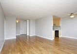 This single-floor unit is designed with a practical, well-organized layout that maximizes functionality throughout. The galley-style kitchen is efficiently arranged with stainless steel appliances, including a refrigerator and electric range, complemented by white cabinetry, grey countertops, a stainless steel sink, and a subtle subway tile backsplash. Light hardwood flooring runs through the kitchen, adding warmth to the space.

The open living area is generously proportioned, featuring the same hardwood flooring, neutral grey walls, and a textured ceiling. A floor-to-ceiling sliding glass door fills the room with natural light and provides direct access to a balcony with outdoor views of surrounding greenery. A baseboard heater runs along the exterior wall. A secondary area off the living space offers additional built-in storage cabinetry.

The bedroom is finished with plush grey carpeting and features a full-width closet with bifold doors, a hanging rod, and a shelf, offering ample storage. The bathroom includes a white vanity with a grey countertop, an undermount sink, and a separate bathtub and shower area, all finished with hardwood-style flooring for a clean, cohesive look.
