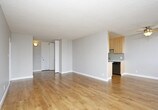 This single-floor unit is designed with a practical, well-organized layout that maximizes functionality throughout. The galley-style kitchen is efficiently arranged with stainless steel appliances, including a refrigerator and electric range, complemented by white cabinetry, grey countertops, a stainless steel sink, and a subtle subway tile backsplash. Light hardwood flooring runs through the kitchen, adding warmth to the space.

The open living area is generously proportioned, featuring the same hardwood flooring, neutral grey walls, and a textured ceiling. A floor-to-ceiling sliding glass door fills the room with natural light and provides direct access to a balcony with outdoor views of surrounding greenery. A baseboard heater runs along the exterior wall. A secondary area off the living space offers additional built-in storage cabinetry.

The bedroom is finished with plush grey carpeting and features a full-width closet with bifold doors, a hanging rod, and a shelf, offering ample storage. The bathroom includes a white vanity with a grey countertop, an undermount sink, and a separate bathtub and shower area, all finished with hardwood-style flooring for a clean, cohesive look.