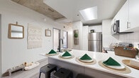 Located in the heart of downtown Denver at 1051 14th St, this single-floor residence offers four bedrooms and three bathrooms with a distinctive industrial-modern aesthetic. Exposed concrete ceilings and visible ductwork provide an urban loft character, while light wood-style flooring and crisp white walls keep the atmosphere bright and contemporary throughout.

The kitchen is a functional centerpiece, featuring stainless steel appliances including a full-size refrigerator, range, and over-the-range microwave. White upper cabinetry contrasts with gray lower cabinets and white countertops, and a skylight overhead adds natural brightness. A peninsula with seating provides a casual dining and gathering space.

The four bedrooms are well-appointed, each carrying the industrial-modern character of the home. Several rooms benefit from large windows that invite natural light and offer city views of the surrounding Denver skyline. The primary bedroom provides a comfortable, intimate retreat.

The three bathrooms are clean and functional, each featuring tub-shower combinations. One bathroom includes a double vanity with ample storage and built-in shelving, lending a shared or en-suite feel. The hallway connecting the bedrooms and bathrooms is well-lit with additional built-in storage. The compact living area adjacent to the kitchen completes this efficient, well-designed urban residence.