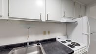 Located at 6 Lamplight Ct in London, Ohio, this single-floor residence offers a straightforward and functional layout designed for comfortable everyday living. The kitchen is efficiently arranged, featuring dark laminate countertops, a stainless steel double-basin sink, white cabinetry with sleek bar-pull hardware, and a coil-burner electric range with an overhead vent. Ample upper and lower cabinet storage keeps the space organized and practical. The living area showcases wood-look vinyl plank flooring and a two-tone wall treatment — crisp white on the upper half and a warm gray on the lower — accented by white chair rail molding and a textured ceiling, creating a clean and understated aesthetic. The bedroom is carpeted for comfort, with neutral white walls and a ceiling light fixture, offering a quiet and restful environment. The full bathroom is finished with wood-look plank flooring, a vanity with a dark countertop and single-basin sink, a large mirror, and a tub-shower combination with a white surround and curved curtain rod. The dollhouse view reveals a compact, well-organized footprint with natural light entering through windows in the main living area, giving the space an open and airy feel.