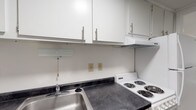Located at 6 Lamplight Ct in London, Ohio, this single-floor residence offers a straightforward and functional layout designed for comfortable everyday living. The kitchen is efficiently arranged, featuring dark laminate countertops, a stainless steel double-basin sink, white cabinetry with sleek bar-pull hardware, and a coil-burner electric range with an overhead vent. Ample upper and lower cabinet storage keeps the space organized and practical. The living area showcases wood-look vinyl plank flooring and a two-tone wall treatment — crisp white on the upper half and a warm gray on the lower — accented by white chair rail molding and a textured ceiling, creating a clean and understated aesthetic. The bedroom is carpeted for comfort, with neutral white walls and a ceiling light fixture, offering a quiet and restful environment. The full bathroom is finished with wood-look plank flooring, a vanity with a dark countertop and single-basin sink, a large mirror, and a tub-shower combination with a white surround and curved curtain rod. The dollhouse view reveals a compact, well-organized footprint with natural light entering through windows in the main living area, giving the space an open and airy feel.
