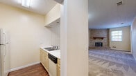 Located at 3113 Cherokee Ave in Columbus, GA, this 2-bedroom, 1-bathroom single-story residence offers a practical and comfortable layout with warm, neutral tones throughout. The living room serves as the heart of the home, highlighted by a striking floor-to-ceiling brick corner fireplace with a classic wood mantel and glass doors, complemented by plush carpet flooring and crown molding. Natural light filters in through windows, adding warmth to the space. The kitchen features light wood cabinetry, light-toned countertops, a double stainless steel sink, and black appliances including a range, microwave, and dishwasher, alongside a full-size refrigerator. A peninsula with a breakfast bar connects the kitchen to the adjoining living area, creating an open, functional flow. Durable hardwood-style flooring runs through the kitchen, while tile flooring is found in the secondary bedroom area. The primary bedroom is a comfortable retreat with carpet flooring, crown molding, a ceiling fan, and direct access to the bathroom and a dedicated closet. The bathroom features tile flooring, a lengthy vanity with ample cabinetry, and a separate water closet for added privacy.