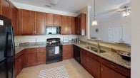 Located at Squires Point in Duncan, South Carolina, this single-floor residence offers a thoughtfully designed layout with a cohesive, neutral color palette and quality finishes throughout. The kitchen is a standout feature, showcasing rich cherry-toned cabinetry, granite countertops, black appliances including a range, refrigerator, and dishwasher, and tile flooring. A pendant light above the sink area adds a decorative touch, while crown molding lends an elevated feel to the space. Adjacent to the kitchen, the dining area benefits from large windows that invite natural light and are accented by a classic multi-bulb chandelier and wainscoting along the walls. The living room is comfortable and open, featuring plush carpet, crown molding, and a seamless flow that connects the main living spaces. Two well-sized bedrooms are finished with carpet flooring, natural light from large windows, and walk-in or reach-in closet access. The bathroom features a granite-topped double vanity with rich cabinetry, a large mirror, and tile flooring consistent with the rest of the home. Throughout the residence, consistent trim work, crown molding, and a warm neutral palette create a unified and welcoming ambiance.