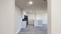 This single-floor residence offers a thoughtfully designed layout encompassing two bedrooms, two bathrooms, and a combined kitchen and living area. The open-concept kitchen and living space serves as the heart of the home, featuring light grey wood-look plank flooring that flows seamlessly throughout. The kitchen is outfitted with tall white shaker-style cabinetry, light-toned quartz countertops, stainless steel appliances including a refrigerator, range, microwave, and dishwasher, and a central island with a built-in sink and pendant lighting above. The expansive living area provides generous room for various furniture arrangements.

Both bedrooms offer comfortable proportions, neutral warm-toned walls, and dedicated closets with built-in shelving. The primary bedroom is particularly spacious, providing ample room for large furnishings. The two bathrooms are finished with tile flooring, white vanities with quartz countertops, and tile-surround soaking tubs. Hallways connect each area efficiently, contributing to a logical and functional flow. The overall aesthetic is clean and modern, with a neutral color palette, recessed lighting, and consistent flooring creating a cohesive and move-in-ready environment throughout.