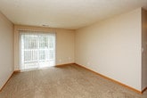 This single-floor residential unit offers a practical and comfortable layout designed for everyday living. The galley-style kitchen is efficiently organized with warm honey-toned wood cabinetry lining both walls, providing generous storage space. It is equipped with standard appliances including an electric range, refrigerator, and dishwasher, along with a double stainless steel sink and light-toned laminate countertops. Light wood-style flooring runs throughout the kitchen, adding warmth to the space.

The living area is generously sized, featuring plush wall-to-wall carpeting and neutral beige walls that create a calm, welcoming atmosphere. A ceiling fan is centrally positioned overhead, and a sliding glass door opens directly to an outdoor balcony or patio, allowing natural light to flow in and providing easy outdoor access.

The bedrooms are carpeted and finished with the same neutral tones, each featuring windows fitted with horizontal blinds that allow for adjustable natural light. The rooms offer comfortable proportions suitable for a range of furniture configurations. Textured ceilings are consistent throughout the unit, and warm wood baseboards provide a cohesive finishing detail across all rooms. The overall layout, as seen in the dollhouse view, reflects a well-structured and functional floor plan with clearly defined living spaces.