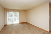This single-floor residential unit offers a practical and comfortable layout designed for everyday living. The galley-style kitchen is efficiently organized with warm honey-toned wood cabinetry lining both walls, providing generous storage space. It is equipped with standard appliances including an electric range, refrigerator, and dishwasher, along with a double stainless steel sink and light-toned laminate countertops. Light wood-style flooring runs throughout the kitchen, adding warmth to the space.

The living area is generously sized, featuring plush wall-to-wall carpeting and neutral beige walls that create a calm, welcoming atmosphere. A ceiling fan is centrally positioned overhead, and a sliding glass door opens directly to an outdoor balcony or patio, allowing natural light to flow in and providing easy outdoor access.

The bedrooms are carpeted and finished with the same neutral tones, each featuring windows fitted with horizontal blinds that allow for adjustable natural light. The rooms offer comfortable proportions suitable for a range of furniture configurations. Textured ceilings are consistent throughout the unit, and warm wood baseboards provide a cohesive finishing detail across all rooms. The overall layout, as seen in the dollhouse view, reflects a well-structured and functional floor plan with clearly defined living spaces.