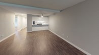This single-floor residence offers a thoughtfully designed layout that balances open living areas with private bedroom spaces. The expansive living room is a standout feature, showcasing dark hardwood-style flooring, soft gray walls, a ceiling fan, and a fireplace framed by a clean white surround. A window allows natural light to filter in, enhancing the room's airy feel.

The kitchen connects seamlessly to the living area via a breakfast bar peninsula. White shaker-style cabinetry pairs with marble-look stone countertops and stainless steel hardware, creating a clean, modern aesthetic. Recessed lighting and a ceiling fan keep the space well-lit and comfortable.

Two bathrooms serve the unit. One features a tub-shower combo, white vanity with marble-look countertop, and wood-look flooring. The second bathroom includes a sliding frosted-glass shower enclosure alongside a vanity and soaking tub.

The bedrooms are carpeted for comfort and finished in neutral gray tones. One bedroom includes a mirrored sliding closet and a baseboard heater beneath a window with outdoor views. The additional bedroom is similarly appointed with a window and baseboard heating. Throughout, the unit maintains a cohesive, contemporary style.