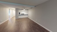 This single-floor residence offers a thoughtfully designed layout that balances open living areas with private bedroom spaces. The expansive living room is a standout feature, showcasing dark hardwood-style flooring, soft gray walls, a ceiling fan, and a fireplace framed by a clean white surround. A window allows natural light to filter in, enhancing the room's airy feel.

The kitchen connects seamlessly to the living area via a breakfast bar peninsula. White shaker-style cabinetry pairs with marble-look stone countertops and stainless steel hardware, creating a clean, modern aesthetic. Recessed lighting and a ceiling fan keep the space well-lit and comfortable.

Two bathrooms serve the unit. One features a tub-shower combo, white vanity with marble-look countertop, and wood-look flooring. The second bathroom includes a sliding frosted-glass shower enclosure alongside a vanity and soaking tub.

The bedrooms are carpeted for comfort and finished in neutral gray tones. One bedroom includes a mirrored sliding closet and a baseboard heater beneath a window with outdoor views. The additional bedroom is similarly appointed with a window and baseboard heating. Throughout, the unit maintains a cohesive, contemporary style.