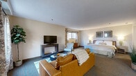 Located at 1001 Bridgeport Avenue in Shelton, CT, this single-floor suite offers a thoughtfully designed layout that maximizes every inch of its living space. The open-concept living area is warm and inviting, featuring plush carpeted flooring, neutral-toned walls, and natural light streaming in through windows dressed with elegant patterned curtains. A flat-screen TV mounted on a media console anchors the living zone, complemented by a leather sofa, accent chairs, and a stylish coffee table.

The kitchen is efficiently designed with white cabinetry, granite countertops, stone tile flooring, and a full suite of appliances including a refrigerator, stove, microwave, and dishwasher. A breakfast bar provides additional seating and counter space, making it functional for both cooking and casual dining.

The generously sized primary bedroom seamlessly integrates a sleeping area with a sitting lounge, offering dual windows, a dresser, and a TV — creating a versatile retreat. Two full bathrooms serve the suite, with one featuring a long granite-topped vanity, warm wood cabinetry, large-format tile flooring, and a full-length mirror. Four closets throughout the suite provide exceptional storage capacity. A hallway connects all areas cohesively, completing this well-organized and comfortable living space.