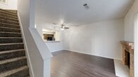 This two-story, 2-bedroom, 2-bathroom home offers a well-organized layout spread evenly across two floors. The main level features a combined living and dining area anchored by a charming brick fireplace and bathed in natural light from a large sliding glass door fitted with vertical blinds. Rich, dark hardwood-style flooring runs throughout the lower level, adding warmth and continuity. The galley-style kitchen is efficiently designed with dark cabinetry, white countertops, black appliances including a refrigerator and electric range, and windows that allow natural light to filter in. A staircase with an open railing leads to the upper floor. The upper level hosts both bedrooms, each equipped with a ceiling fan, plush carpeting, and windows with blinds for natural light and privacy. The primary bedroom includes access to a closet and is generously proportioned. Both bathrooms feature dark cabinetry vanities with white countertops, large mirrors, and hardwood-style flooring. Additional highlights include multiple closets for ample storage, a dedicated laundry area, a hallway connecting the upper-level rooms, and a textured ceiling throughout. The layout is practical and functional, making efficient use of the available space across both levels.