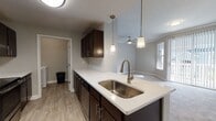 This well-appointed apartment showcases a blend of style and functionality. The kitchen boasts dark wood cabinetry, stainless steel appliances, and a chevron tile backsplash. Living spaces are bright and airy, with plush carpeting and ample natural light from large windows. Bathrooms feature modern fixtures and wood-look tile flooring. The unit includes a dedicated laundry area with full-size washer and dryer. Generous closet space with wire shelving provides ample storage. The overall design creates a cohesive and inviting living environment with a contemporary aesthetic.