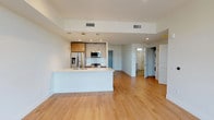 This single-floor residence showcases a clean, modern design with an open-concept layout that connects the living area and kitchen seamlessly. The living space features warm hardwood flooring, recessed lighting, and large floor-to-ceiling sliding glass doors that open onto a private balcony, flooding the area with natural light and offering views of the surrounding neighborhood and cityscape.

The kitchen is well-appointed with stainless steel appliances, including a gas range, built-in microwave, and French door refrigerator. A geometric-patterned tile backsplash adds visual interest, while warm wood cabinetry is paired with crisp white upper cabinets. A generous island with a quartz countertop and undermount sink provides ample workspace and serves as a natural gathering point.

The two bedrooms are carpeted for comfort and feature large windows with outdoor views, providing excellent natural light. One bedroom benefits from a dedicated walk-in closet with built-in shelving and hanging rods. The bathroom is finished with large-format tile flooring, a frameless glass walk-in shower with white tile surround, and a floating vanity with a clean-lined mirror. In-unit laundry is conveniently tucked within the unit, completing this thoughtfully designed residence.