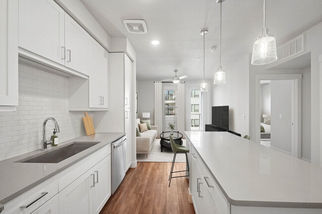 Finish Package II kitchen with stainless steel appliances, white cabinetry, white tile backsplash, grey quartz countertops, and hard surface flooring - Avalon Lowry