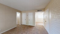 This single-story residential unit offers a functional and well-organized layout spread across multiple rooms. The living room serves as the welcoming centerpiece of the space, featuring a painted white brick accent wall that adds architectural character, neutral beige carpeting, and a window fitted with blinds that allows natural light to filter in. Two interior doors in the living area provide access to additional rooms and closet storage.

The galley-style kitchen is efficiently designed, with white cabinetry lining both walls and light-toned countertops offering ample workspace. The kitchen is equipped with a gas range, black refrigerator, and dishwasher, all set above warm hardwood-style flooring. A flush-mount ceiling light provides overhead illumination.

The bedrooms are carpeted and finished in soft neutral tones, each offering closet access and ceiling fan fixtures. The primary bedroom features multiple closet doors and connects to a hallway leading to additional areas of the home.

Two full bathrooms serve the unit, each featuring a tiled tub-and-shower combination with warm-toned tile surrounds. One bathroom includes hardwood-style flooring, while the other features tile. Both are finished with textured walls and chrome fixtures. Throughout the home, textured ceilings, white trim, and a consistent neutral palette create a cohesive and understated aesthetic.
