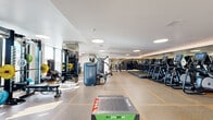 Located at 200 Mesnagers St in Los Angeles, CA, this single-floor fitness center offers a generously sized, open exercise space designed to accommodate a full range of workout needs. The room features a clean, contemporary aesthetic with crisp white walls, smooth white ceilings with recessed circular lighting fixtures, and durable speckled rubber flooring that provides both traction and comfort underfoot.

The cardio zone is anchored by a long row of treadmills and elliptical machines lined against a full-length mirror wall, which amplifies the sense of space and allows users to monitor their form during workouts. Natural light filters in through large windows along the perimeter, creating a bright and energizing atmosphere.

The strength training area is equally well-appointed, featuring a power rack loaded with barbells and weight plates, a comprehensive dumbbell rack with a wide range of free weights, and multiple cable and resistance machines suited for targeted muscle training. A dedicated multi-use cable system with suspension attachments supports functional and cross-training exercises.

The layout is thoughtfully organized to separate cardio and strength zones, ensuring an efficient flow throughout the space. Mirror panels are strategically placed to enhance visibility and openness. Overall, this fitness center delivers a professional-grade workout environment with a polished, modern design.