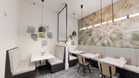 Located at 2410 Canopy Breeze Circle in Orlando, FL, this single-floor space offers a thoughtfully designed interior that blends modern aesthetics with comfortable functionality. The dining area is anchored by plush, light-textured banquette booths and marble-top tables, creating an inviting atmosphere suited for casual gatherings or intimate meetings. Dark-framed pendant lights with matte black and gold accents hang overhead, providing warm, focused illumination that complements the space's refined palette of whites, grays, and earthy tones. A striking large-scale botanical wall mural — depicting a close-up of a dandelion — serves as a dramatic focal point, adding an organic, nature-inspired element to the contemporary interior. Textured stone tile art pieces are arranged in a grid pattern along the white walls, contributing an additional layer of visual interest. The floors are finished with a patterned blue-gray carpet that grounds the space with depth and texture. A glass-paneled partition wall and a glass-door entry provide visual connectivity to adjacent areas, including a bay office space visible beyond, ensuring the space feels open and cohesive while maintaining distinct zones. The overall ambiance is polished, modern, and welcoming.