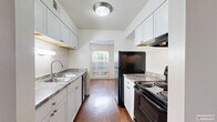 This single-story, 2-bedroom, 1-bathroom residence offers a functional and comfortable layout across a well-utilized floor plan. The living room serves as the heart of the home, featuring warm hardwood-style flooring, neutral white walls, and a sliding glass door that floods the space with natural light while providing direct access to a greenery-filled outdoor patio. Adjacent to the living area, a dedicated dining room offers a seamless transition into the galley-style kitchen, which is equipped with white cabinetry, granite-style countertops, a double-basin sink, and black appliances including a range, dishwasher, and refrigerator. A window at the far end of the kitchen brings in additional natural light. Both bedrooms are carpeted and feature ceiling fans, windows with outdoor views, and generous closet space — the primary bedroom includes a dedicated closet, while the secondary bedroom benefits from dual sliding-door closets. A utility room with laundry hookups adds everyday convenience. The full bathroom is finished with a clean white vanity, hardwood-style flooring, and a full tub-shower combination. A hallway connects the private areas of the home, and five total closets throughout ensure exceptional storage capacity.