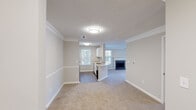 This single-floor residence offers a thoughtfully designed open-concept layout that seamlessly connects the living, dining, and kitchen areas. The living room is a welcoming focal point, highlighted by a tile-surround fireplace framed with a classic white mantel, plush carpeting, crown molding, and a ceiling fan. Multiple windows flood the space with natural light, while a set of French doors opens directly onto a private outdoor deck, offering pleasant outdoor views.

The kitchen is both functional and stylish, featuring white cabinetry — including a distinctive lattice-detail wine rack cabinet — stainless steel appliances including a refrigerator, electric range, and built-in microwave, as well as a light-toned countertop peninsula with a double undermount sink and a contemporary gooseneck faucet. Wood-look flooring in the kitchen transitions smoothly to carpeted living areas. Crown molding and chair rail detailing carry throughout the main living spaces, lending a refined, cohesive aesthetic.

The bathroom includes a full soaking tub with a tiled shower surround in clean, bright white. Overall, the space maintains a neutral, light palette throughout, creating a bright and inviting atmosphere well-suited for comfortable everyday living.