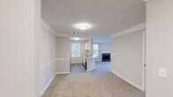 This single-floor residence offers a thoughtfully designed open-concept layout that seamlessly connects the living, dining, and kitchen areas. The living room is a welcoming focal point, highlighted by a tile-surround fireplace framed with a classic white mantel, plush carpeting, crown molding, and a ceiling fan. Multiple windows flood the space with natural light, while a set of French doors opens directly onto a private outdoor deck, offering pleasant outdoor views.

The kitchen is both functional and stylish, featuring white cabinetry — including a distinctive lattice-detail wine rack cabinet — stainless steel appliances including a refrigerator, electric range, and built-in microwave, as well as a light-toned countertop peninsula with a double undermount sink and a contemporary gooseneck faucet. Wood-look flooring in the kitchen transitions smoothly to carpeted living areas. Crown molding and chair rail detailing carry throughout the main living spaces, lending a refined, cohesive aesthetic.

The bathroom includes a full soaking tub with a tiled shower surround in clean, bright white. Overall, the space maintains a neutral, light palette throughout, creating a bright and inviting atmosphere well-suited for comfortable everyday living.