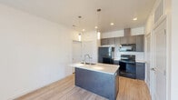 Located at 2120 W A St in Pasco, WA, this well-designed one-bedroom, one-bathroom unit offers a thoughtful, efficient layout with modern finishes throughout. Light wood-tone flooring runs continuously across the entire space, creating a cohesive and clean aesthetic.

The kitchen serves as the centerpiece of the open living area, anchored by a substantial island with a white quartz countertop, an integrated sink, and stylish pendant lighting overhead. Gray shaker-style cabinetry lines the walls, complemented by a white subway tile backsplash and black stainless steel appliances, including a refrigerator, electric range, and microwave. Recessed lighting enhances the bright, airy atmosphere.

The bedroom is generously proportioned and features multiple windows that invite abundant natural light and provide outdoor views of the surrounding community. The clean white walls and light flooring contribute to a calm, restful environment.

The bathroom includes a full soaking tub and shower combination with brushed nickel fixtures, maintaining the unit's consistent modern style. A dedicated in-unit laundry room provides added convenience, housing a full-size washer and dryer with shelving above. The overall design is contemporary, clean, and functional, offering comfortable everyday living.