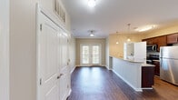 Located along Providence Main Street NW in Huntsville, Alabama, this one-bedroom, one-bathroom residence offers a thoughtfully designed layout across a single floor. Rich, dark hardwood-style flooring runs throughout the main living areas, creating a warm and cohesive aesthetic. The open living room is bathed in natural light, courtesy of French doors that invite the outdoors in, and is complemented by crown molding and a ceiling fan overhead.

The kitchen is a functional highlight, featuring rich dark cabinetry, granite countertops, stainless steel appliances — including a refrigerator, range, and microwave — and a breakfast bar with pendant lighting that flows seamlessly into the living space. A dedicated laundry room with shelving and a window providing natural light adds everyday convenience.

The generously sized bedroom is carpeted for comfort, with a ceiling fan, ample natural light from large windows, and direct access to the bathroom. The bathroom is well-appointed with dark wood vanity cabinetry, stone-topped counters, a large mirror, and a tub-shower combination set over light tile flooring. Throughout the residence, neutral tones and clean finishes create a bright, inviting ambiance ideal for comfortable everyday living.