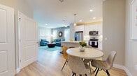 This single-floor residence in Davenport, Florida offers a well-designed open-concept layout that seamlessly connects the kitchen, dining, and living areas. Light wood-tone flooring runs throughout, lending warmth and continuity to the entire space.

The kitchen is outfitted with white shaker cabinetry, a subway tile backsplash, quartz countertops, and a full suite of stainless steel appliances, including a French door refrigerator, range, microwave, and dishwasher. Open shelving adds both function and visual interest. A peninsula with seating serves as a natural divider between the kitchen and the adjacent dining area, which accommodates a round table for casual meals.

The living room is bright and welcoming, with multiple windows dressed in white blinds that allow generous natural light. The space flows effortlessly from the entry, creating an airy, open feel.

The bedroom features a ceiling fan, a large window with natural light, and access to a clean, white bathroom complete with shaker-style vanity cabinetry, quartz countertops, and a shower. The overall aesthetic throughout is fresh, coastal-modern, and cohesive.