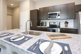 Located at 6848 Governors West NW in Huntsville, Alabama, this single-story residence offers a thoughtfully designed layout with modern finishes and functional living spaces. The open-concept kitchen serves as a central hub, showcasing dark espresso cabinetry, granite countertops, a large island with seating for multiple guests, subway tile backsplash, and a full suite of stainless steel appliances. Light wood-style flooring runs throughout the main living areas, complementing the neutral color palette.

The living area provides a comfortable and stylish setting with soft, neutral walls and ample space for relaxed gatherings. Multiple bedrooms feature plush carpeting, ceiling fans, natural light from well-positioned windows, and access to dedicated closets. The primary bedroom includes a walk-in closet and an en-suite bathroom with a dark vanity, granite countertop, and wood-look flooring. Additional bathrooms mirror this refined aesthetic with matching fixtures and finishes.

A dedicated laundry room, conveniently accessible from the kitchen, houses a full-size washer. Closets throughout offer practical storage solutions. The cohesive design and quality finishes combine to create a polished, comfortable living environment.