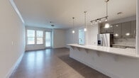 This single-floor residence offers a clean, contemporary design with a cohesive aesthetic throughout. The heart of the home is an open-concept kitchen and living area, where a sleek peninsula with a white quartz countertop and built-in sink serves as a natural focal point. The kitchen is equipped with stainless steel appliances — including a French door refrigerator, electric range, and built-in microwave — complemented by gray cabinetry, a marble-style tile backsplash, and pendant lighting overhead. The expansive living area flows seamlessly from the kitchen, featuring wood-look flooring and large windows that invite abundant natural light. The bedrooms continue the light, neutral palette with the same wood-look flooring, ample wall space, and access to natural light. The primary bedroom connects to a generously sized en-suite bathroom, which includes a dual-sink vanity with quartz countertops, a soaking tub, and a separate glass-enclosed shower. A second full bathroom offers a tub-shower combination with white tile surround and an overhead storage cabinet. Throughout the space, white walls, clean trim, and consistent flooring create a bright, airy ambiance suited to modern living.