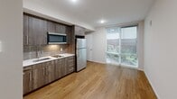 Located at 1420 E Howell St, Unit 106 in Seattle's Capitol Hill neighborhood, this studio unit offers an efficient and modern single-floor layout. The combined kitchen and living area serves as the heart of the space, featuring warm hardwood-style flooring, neutral wall tones, and a large sliding window that draws in natural light and offers a view of outdoor greenery. The kitchen is well-appointed with dark wood cabinetry, a tile backsplash, a stainless steel refrigerator, a built-in microwave, and a sink — all arranged in a clean, linear configuration that maximizes functionality without compromising the open feel of the living area. A closet provides dedicated storage, keeping the living space uncluttered. The bathroom is finished with large-format gray tile flooring and white wall tiles, punctuated by a decorative vertical mosaic tile accent in earthy greens and grays above the bathtub — adding a distinct visual element to the otherwise clean, minimalist design. Recessed and flush-mount lighting throughout ensures the space remains bright and functional. The overall aesthetic is modern and practical, thoughtfully designed to make the most of every square foot.