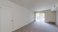 This single-floor residence offers a practical and comfortable layout designed to maximize functionality throughout. The living room is generously proportioned, finished with plush wall-to-wall carpeting and crisp white walls that create a bright, airy atmosphere. A full-height sliding glass door with vertical blinds fills the space with natural light and provides direct access to the outdoors, offering views of surrounding greenery. An additional door nearby adds convenient connectivity within the unit.

The galley-style kitchen is well-appointed with dark espresso cabinetry, light granite-style countertops, and wood-look plank flooring that adds warmth and durability. A stainless steel sink, gas range, and full-size refrigerator complete the functional cooking space, with ample upper and lower cabinet storage throughout.

The bedroom is a calm, carpeted retreat with a large window that frames outdoor tree views and allows natural light to pour in. The room offers a quiet, restful ambiance with neutral tones throughout.

The bathroom features classic white mosaic tile flooring, a full-size soaking tub with an overhead shower, and a dark-toned vanity that provides a subtle contrast to the clean white walls and fixtures. The overall design of the space is clean, neutral, and move-in ready.
