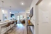 Located at 1 Henry Circle in Flagler Beach, Florida, this well-appointed 2-bedroom, 2-bathroom single-floor residence offers a thoughtfully designed open-concept layout with a bright, contemporary aesthetic. Wood-look flooring flows throughout the space, tying together each room cohesively.

Upon entering, a welcoming hallway leads into the combined kitchen and living area. The kitchen is equipped with stainless steel appliances, including a full-size refrigerator, electric range, and over-the-range microwave, complemented by light wood cabinetry, granite-style countertops, open shelving, and a breakfast bar with seating. The living area is bathed in natural light from large windows and a glass door that opens to the outdoors, creating an airy and inviting atmosphere. A ceiling fan adds to the comfort of the space.

The primary bedroom is a generously sized retreat featuring a ceiling fan, clean white walls, and direct access to a walk-in closet outfitted with wire shelving. The bathrooms are finished with granite-topped vanities and tub-shower combinations. A dedicated in-unit laundry room houses a full-size washer and dryer with overhead wire shelving for added storage. Two closets throughout the home provide ample organizational space.