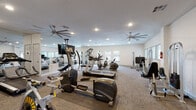 This fitness center offers a comprehensive workout environment thoughtfully designed to support a wide range of exercise routines. The main gym area is generously proportioned and features a curated selection of cardio equipment, including treadmills, elliptical trainers, and stationary cycling bikes from brands such as Schwinn. Strength training is supported by a cable machine, a dumbbell rack with free weights, and additional resistance equipment. Large wall-to-wall mirrors line key areas of the facility, visually expanding the space and allowing users to monitor their form during workouts. Overhead, multiple large ceiling fans promote air circulation throughout the room, complemented by recessed lighting that keeps the environment bright and inviting. Neutral-toned carpet flooring and protective rubber mats beneath equipment contribute to a clean, functional aesthetic. Natural light filters in through multiple windows, offering views of surrounding greenery and enhancing the overall atmosphere. A separate studio room adjoins the main fitness floor, featuring floor-to-ceiling mirrors along one wall and a row of windows that flood the space with natural light — ideal for yoga, stretching, or group fitness activities. The facility's clean, modern design and well-maintained equipment make it a practical and welcoming space for daily exercise.