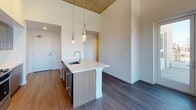This two-bedroom residence showcases a contemporary industrial-modern design highlighted by dramatic ceiling heights and rich dark hardwood-style flooring throughout. Exposed concrete columns and raw ceiling details add an urban character, contrasting elegantly with the crisp white walls.

The open-concept kitchen is a standout feature, centered around a large island with a white quartz countertop, undermount sink, and stylish pendant lighting overhead. Warm wood-toned cabinetry lines the walls, complemented by a full suite of stainless steel appliances including a refrigerator, range, and microwave.

Both bedrooms are generously proportioned, each benefiting from large windows that frame expansive city skyline views, flooding the rooms with natural light. One bedroom offers multiple closets, providing ample storage. The two bathrooms are cleanly finished with wood-look flooring, neutral tile surrounds, and modern fixtures. A dedicated in-unit laundry area with a stacked washer and dryer adds convenience. The overall ambiance is polished and urban, combining industrial architectural elements with modern, refined finishes.