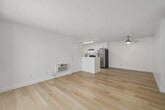 This 2-bedroom, 2-bathroom residence offers a clean, contemporary aesthetic throughout its efficiently designed single-floor layout. Light-toned hardwood flooring runs consistently through every room, creating a sense of warmth and continuity across the entire space.

The combined living room and kitchen area forms the heart of the home. The living room is bright and open, featuring a textured ceiling, a wall-mounted HVAC unit, and a sliding glass door that opens onto a private balcony with views of surrounding rooftops and mature trees. The galley-style kitchen is outfitted with crisp white cabinetry extending to the ceiling, white quartz countertops, a stainless steel sink with a modern pull-down faucet, a dishwasher, electric range, and a full-size refrigerator, all illuminated by overhead recessed lighting.

The primary bedroom is generously proportioned and features a large window with vertical blinds that invites abundant natural light. It includes an open closet with built-in shelving, providing practical storage. The second bedroom offers a similarly clean and bright environment. Both bathrooms are finished in an all-white palette with tub-shower combinations, white vanities, and modern chrome fixtures. Two hallways connect the rooms efficiently, completing this well-organized and move-in-ready layout.